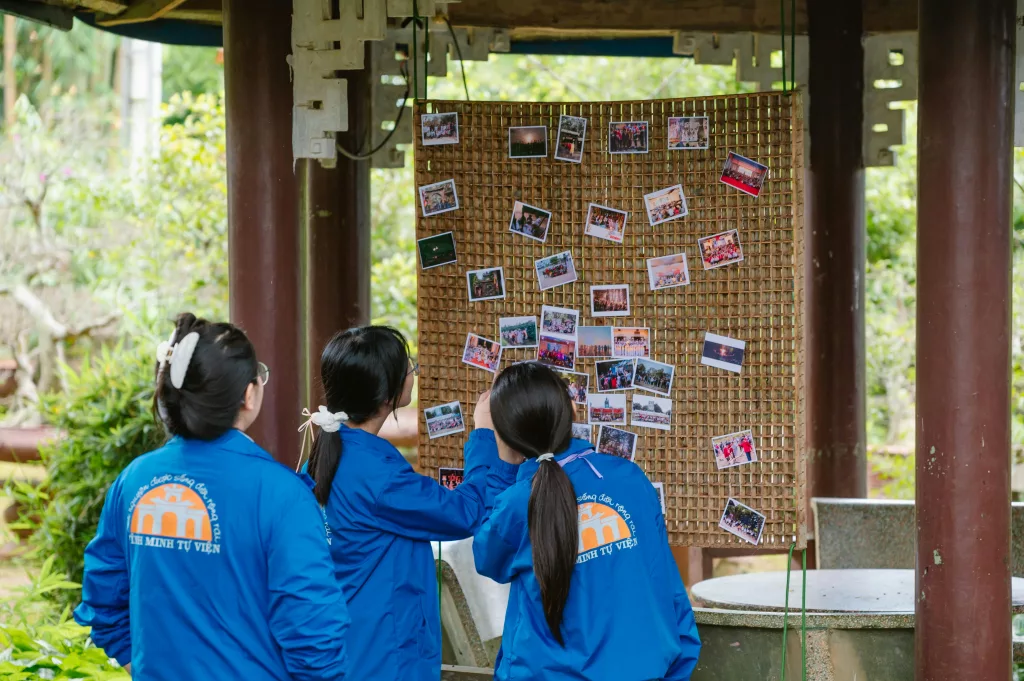 Group of teenagers in blue jackets viewing a pinned photo display in an outdoor setting.